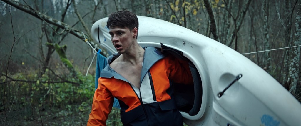 Andrejs (Igors Selegovskis) carrying a kayak, looking disheveled.