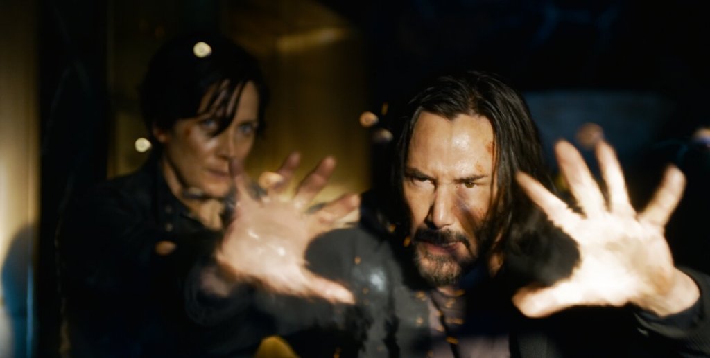 Neo (Keanu Reeves) stopping bullets with his hands/mind. Trinity (Carrie-Anne Moss) standing behind him.