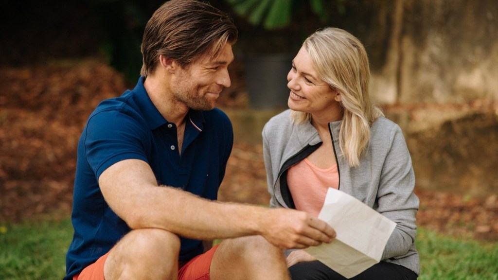 Chip (Liam McIntyre) and Laura (Saskia Hampele) reading something together, smiling at each other.