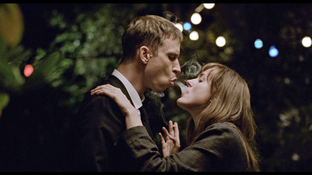 Julie (Renate Reinsve) and Eivind (Herbert Nordrum) smoking a cigarette together. He is blowing smoke into her mouth.