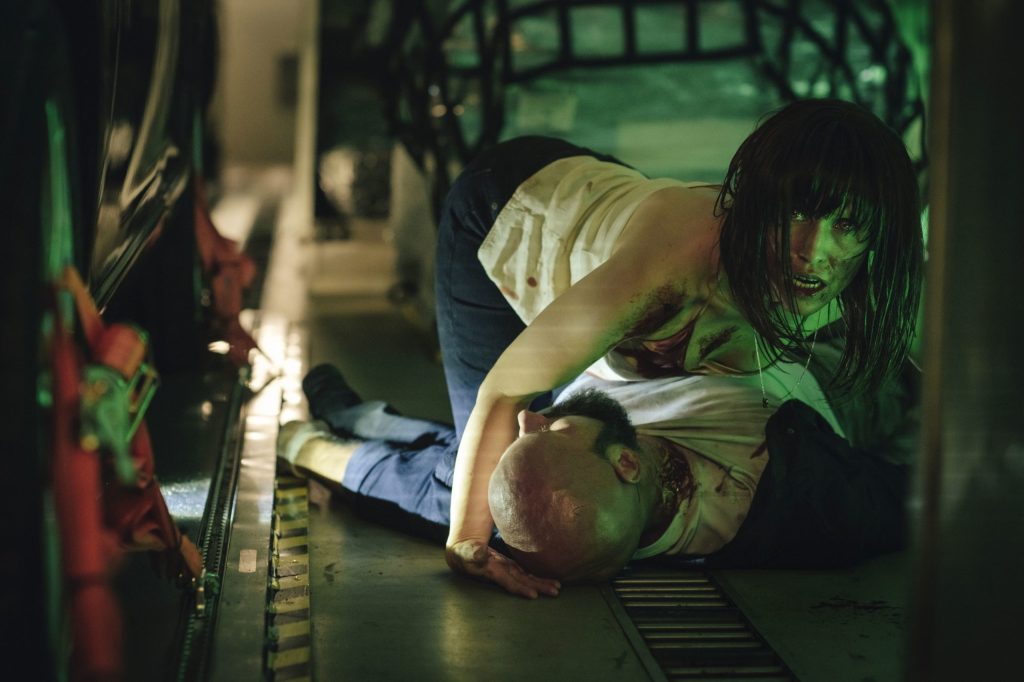 Nadja (Peri Baumeister) leaning over a guy lying dead on the floor. Her face is subtly changed, her face and his neck are bloody.