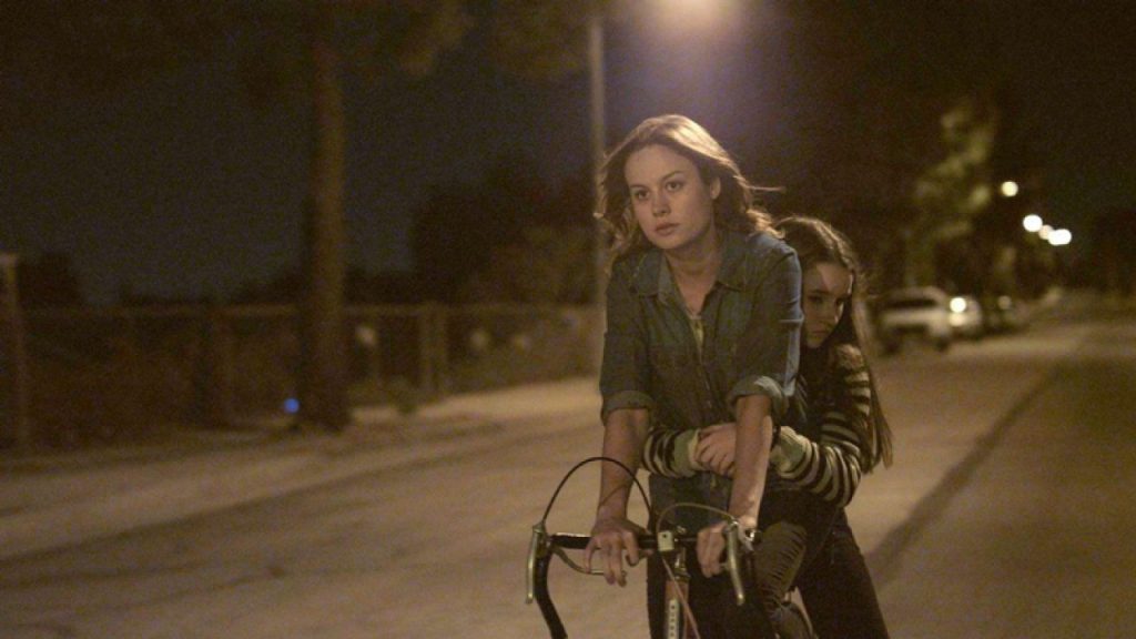 Grace (Brie Larson) cycling with Jayden (Kaitlyn Dever) on the carrier behind her
