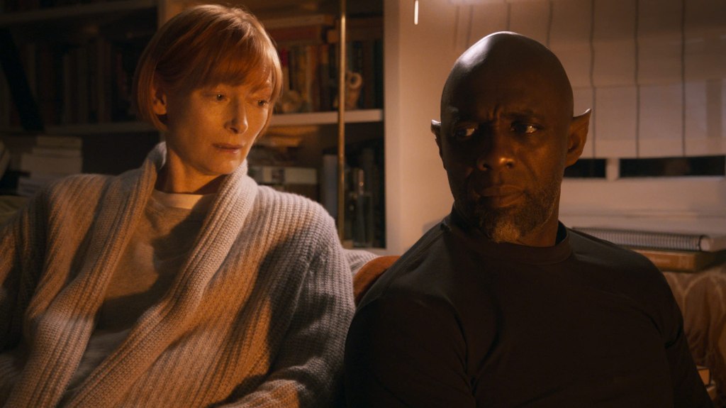 Alithea (Tilda Swinton) and the Djinn (Idris Elba) sitting on the sofa together.