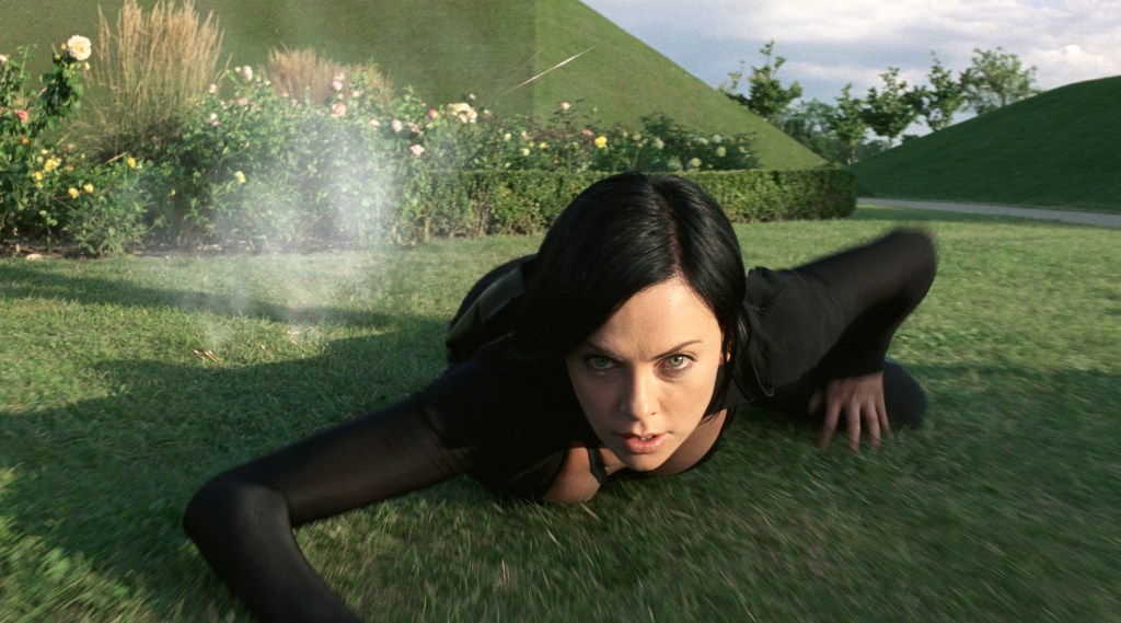 Æon (Charlize Theron) crawling over grass that is releasing a toxic vapor.