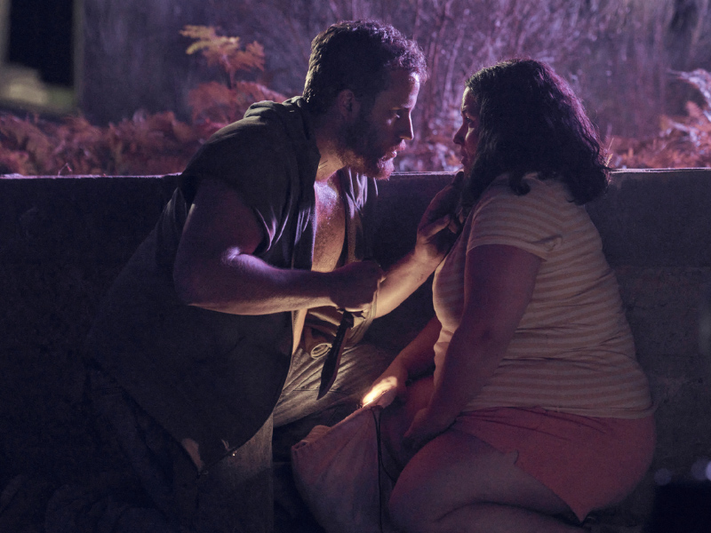 Sara (Laura Galán) huddled together with a man (Richard Holmes). He is holding a large knife.