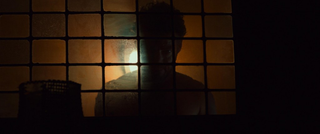 A silhouette behind a dimly lit window.
