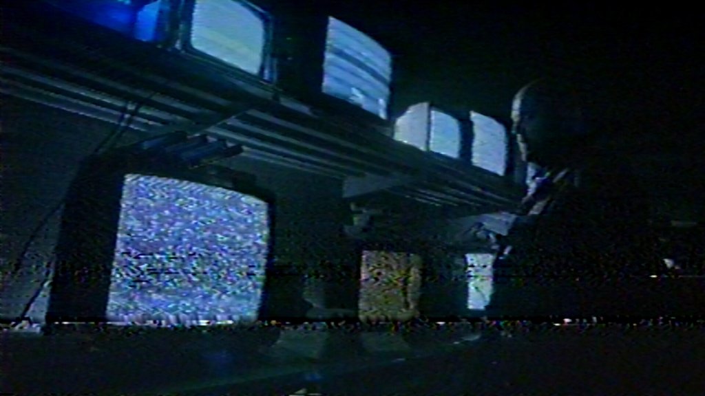 A man standing in front of several old TVs, all showing static.