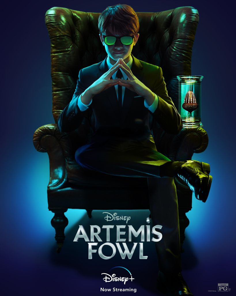 The film poster showing Artemis Fowl (Ferdia Shaw) sitting in an arm chair, his fingers stapled, wearing a suit and sunglasses. Next to him is a giant shiny acorn in a special container.