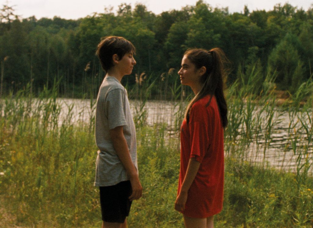Bastien (Joseph Engel) and Chloe (Sara Montpetit) looking at each other on the lake shore.