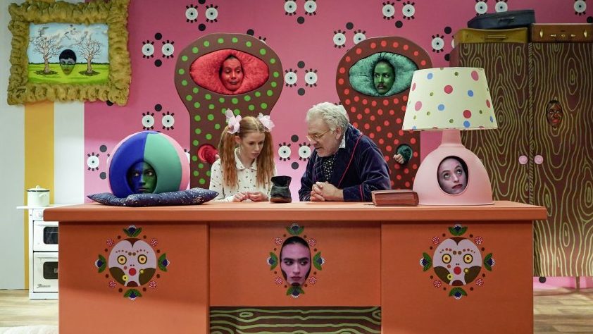 The child (Hani Furstenberg) and the storyteller (Jeff Francis) looking intently at a boot in the colorful set of the show.