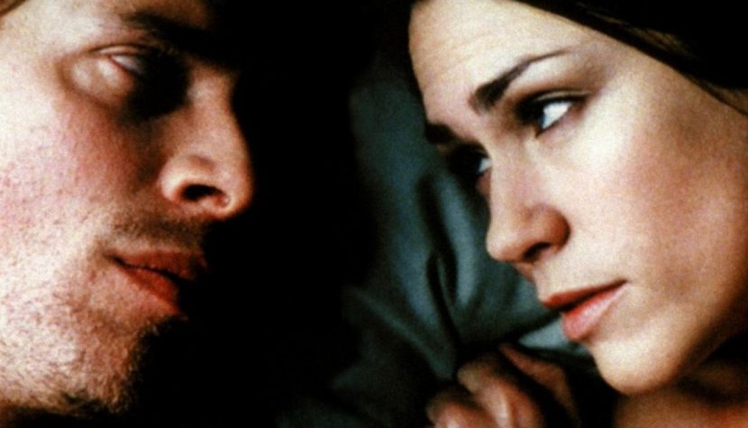 Evian (Jean-Nicolas Verreault) and Bibiane (Marie-Josée Croze) lying in bed together, looking at each other.