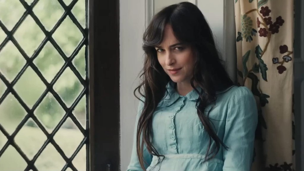 Anne (Dakota Johnson) sitting at the window, looking straight into the camera.