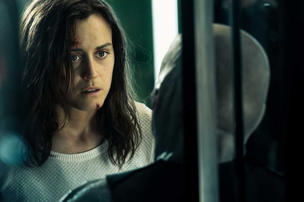 Abi (Taylor Schilling), looking quite banged up, looking at a very changed Rick (Sam Worthington). 