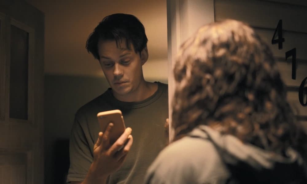 Keith (Bill Skarsgård) looking confused at Tess' (Georgina Campbell) phone in the doorway of the rental house.