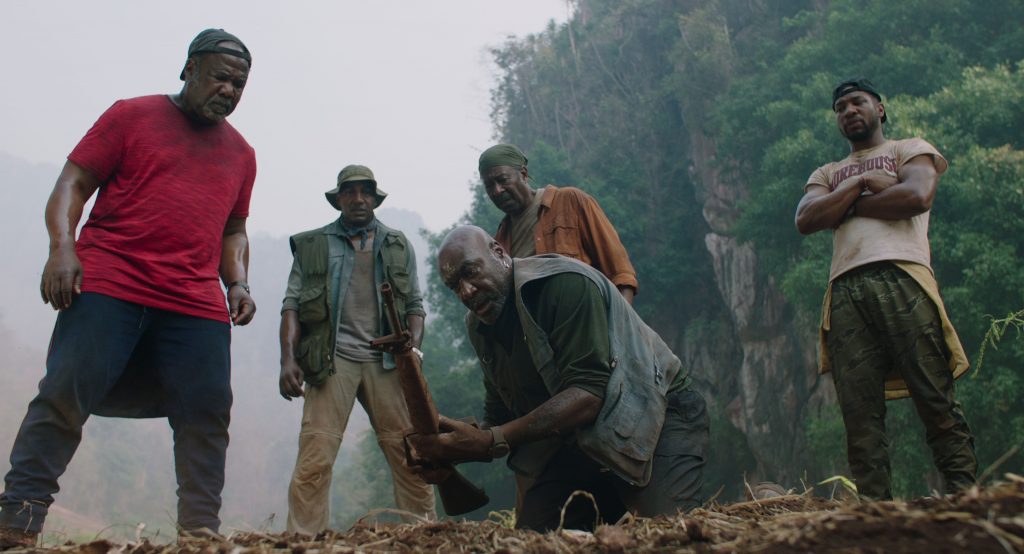 Melvin (Isiah Witlock Jr.), Eddie (Norm Lewis), Otis (Clarke Peters) and David (Jonathan Majors) standing behind Paul (Delroy Lindo) who is picking up a gun from the ground.
