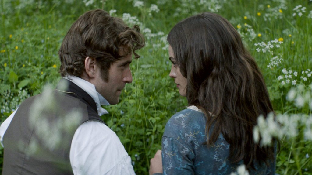 William (Oliver Jackson-Cohen) and Emily (Emma Mackey) sitting in the grass together.