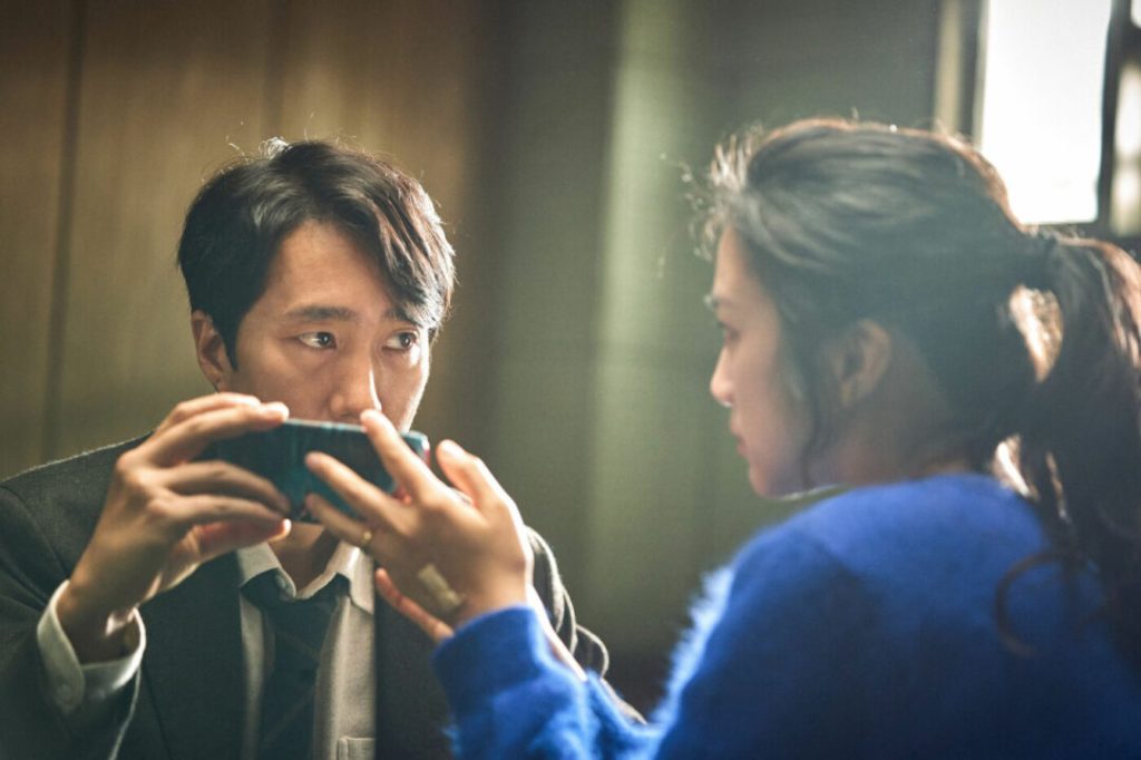 Jang Hae-joon (Park Hae-il) and Song Seo-rae (Tang Wei) in the interrogation room, looking at a phone.