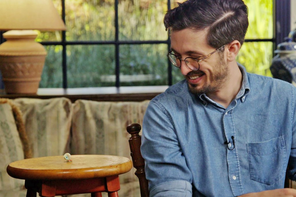 Marcel on a stool next to Dean (Dean Fleischer Camp) who smiles at him.