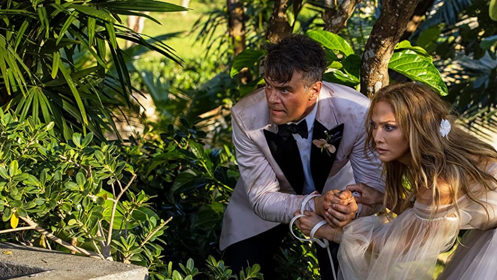 Tom (Josh Duhamel) and Darcy (Jennifer Lopez) cowering in the bushes, their hands tied together.