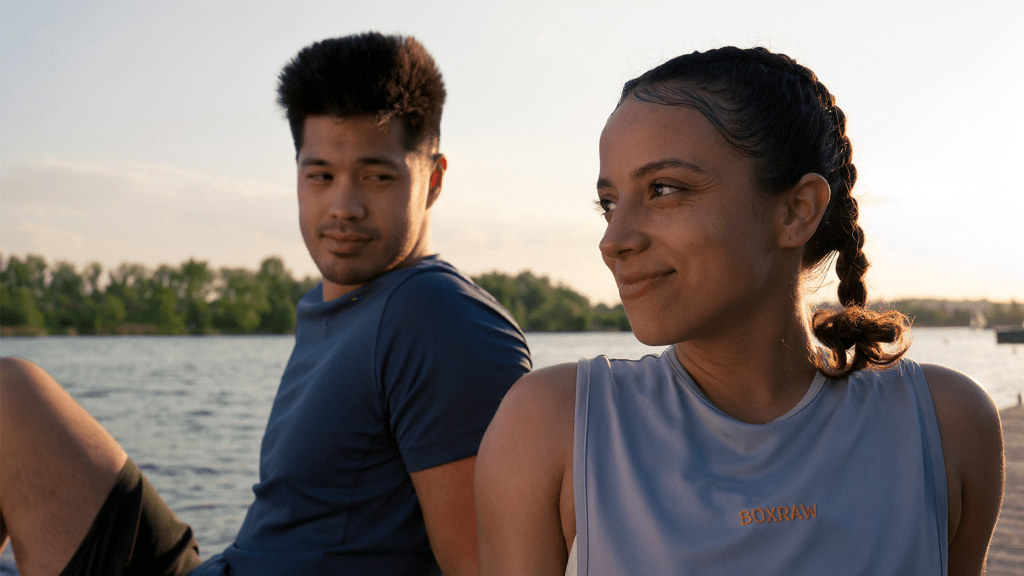 Kayden (Ross Butler) and Sienna (Kiana Madeira) taking a break from training next to a lake.