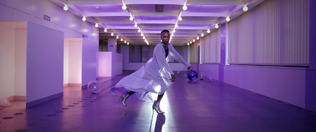 A dancer in high heels dancing in a room that is lit in purple.