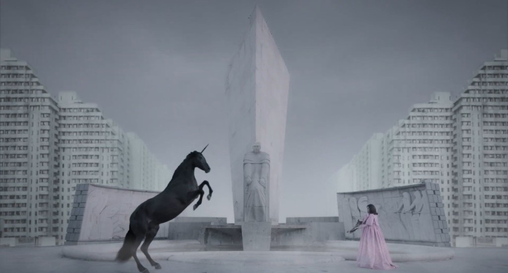 Lili (Ángela Molina) aiming a crossbow at a black unicorn in a white dreamscape.