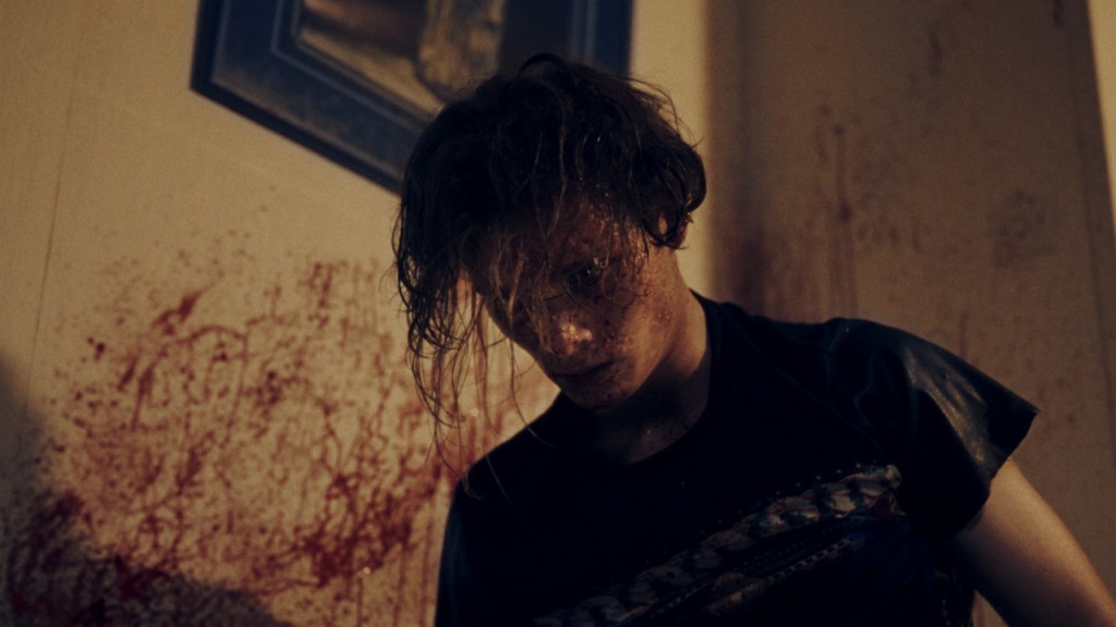 A blood-speckled young man leaning over something. 