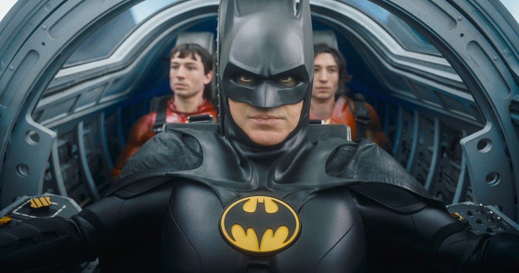 Batman (Michael Keaton) riding in a bat vehicle with two versions of Barry Allen (both: Ezra Miller).