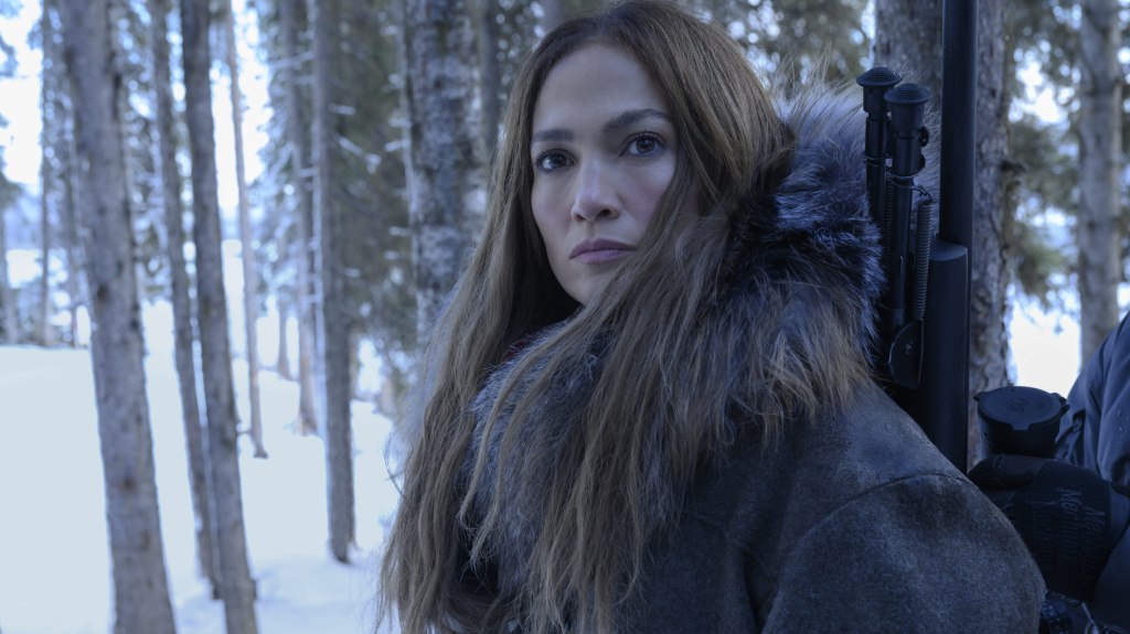The Mother (Jennifer Lopez) in a snowy forest, a rifle strapped to her back.