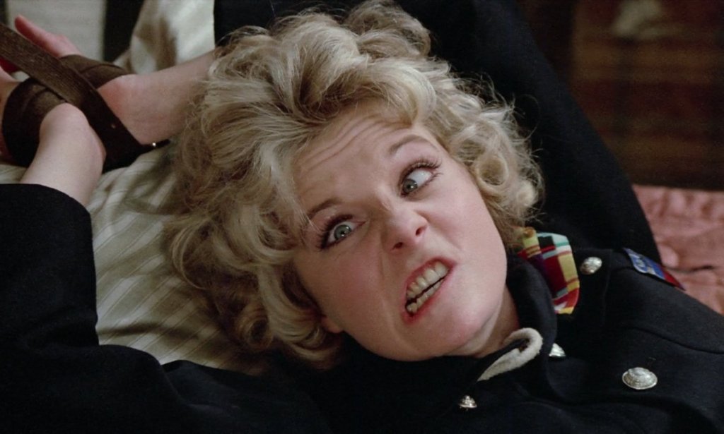 Cookie (Sheila White) tied to a bed, grimacing.