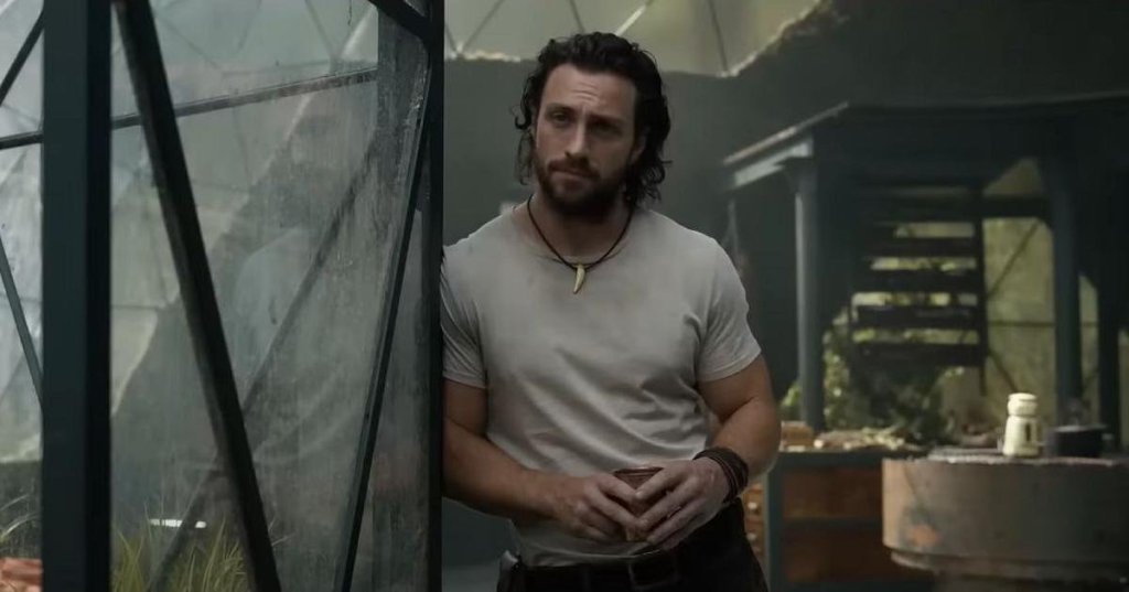 Sergei aka Kraven (Aaron Taylor-Johnson) leaning against a glass terrarium.