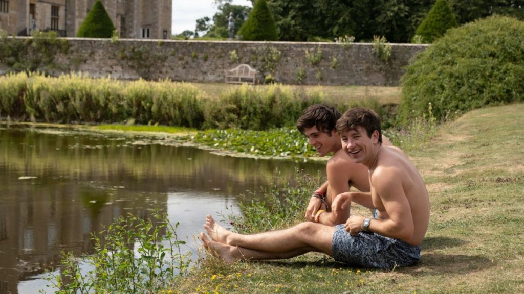 Felix (Jacob Elordi) and Oliver (Barry Keoghan) sitting next to a pond, laughing.