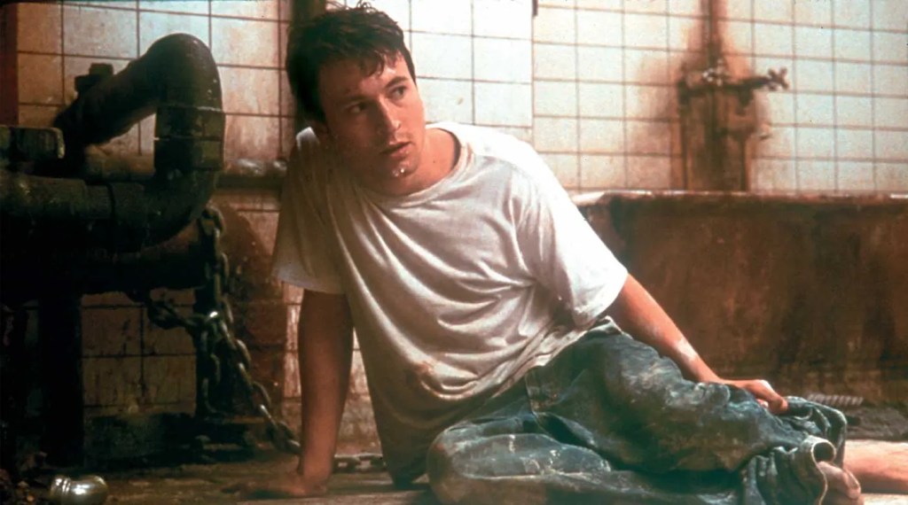 Adam (Leigh Whannell) sitting on the floor of a dilapitated bathroom, chained to the wall.