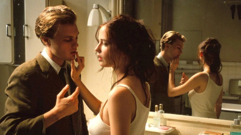 Matthew (Michael Pitt) and Isabelle (Eva Green) standing in a bathroom. She is pushing her finger against his lips.