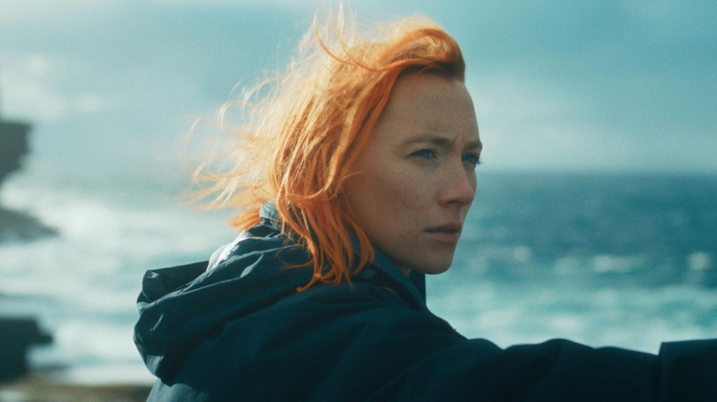 Rona (Saoirse Ronan), her hair dyed orange and blowing in the wind, looking out to sea.