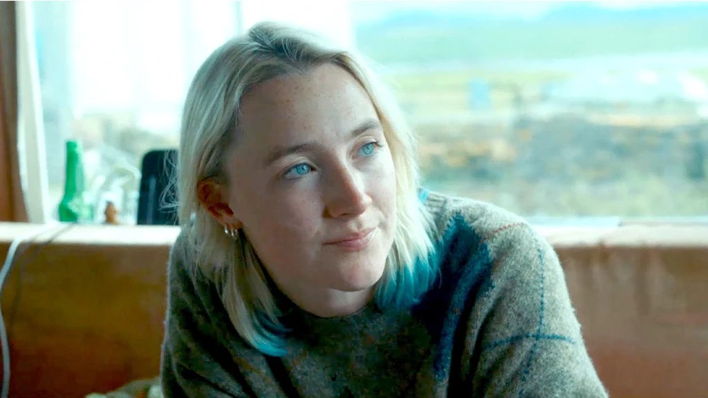 Rona (Saoirse Ronan), hair blond with blue tips, sitting on a sofa.