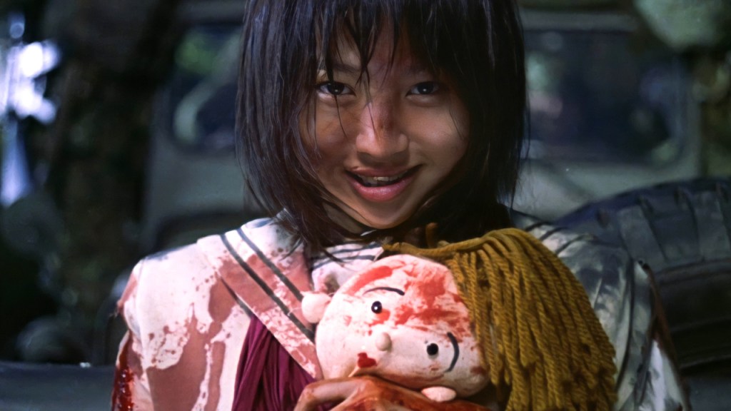 A girl clutching a doll, both splattered in blood. She is smiling.