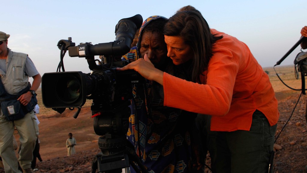 Kirsten Johnson looking through a camera together with an African men, surrounded by film crew.