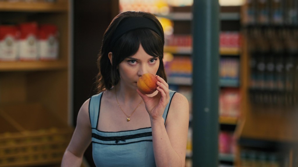 Iris (Sophie Thatcher) smelling a peach in a supermarket.