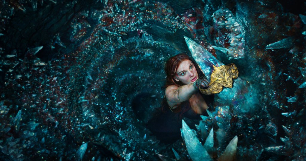 Elodie (Millie Bobby Brown) hanging from what looks like a sharp crystal, maybe a tooth over a maw filled with its like. 