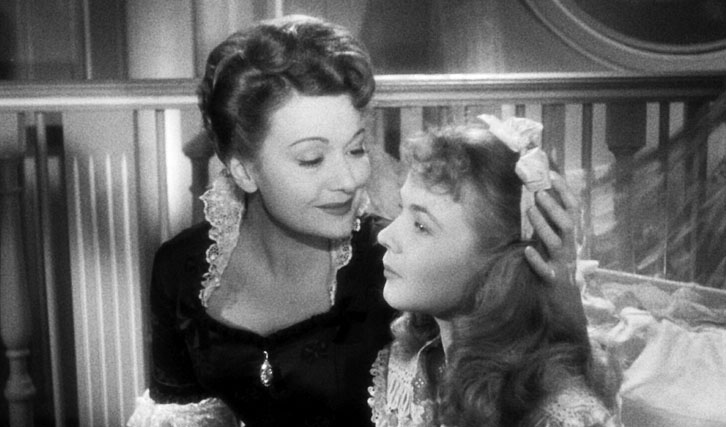 Julie (Edwige Feuillère) sitting at the edge of Olivia's (Marie-Claire Olivia) bed, cradling her head.