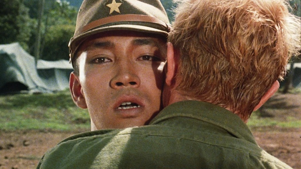Celliers (David Bowie) embracing Yonoi (Ryuichi Sakamoto) who looks stunned.