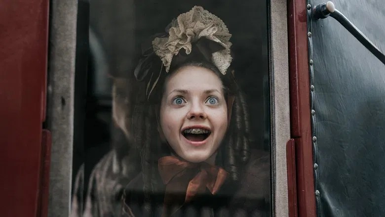 Elvira (Lea Myren) looking excitedly out of a carriage. Her hair-do is unfortunate and she is wearing braces. 