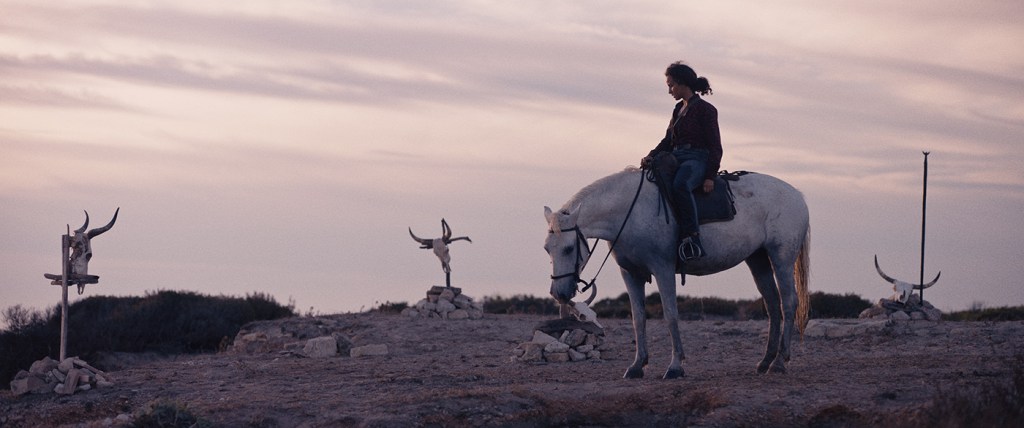 Nejma (Oulaya Amamra) on horseback standing amidst a few graves topped by bull skulls. 