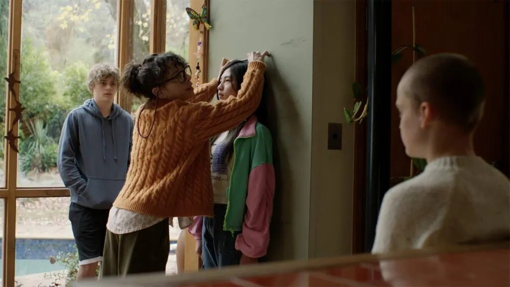 Laura (Sally Hawkins) measuring Piper's (Sora Wong) height against a wall, as Oliver (Jonah Wren Phillips) and Andy (Billy Barratt) look on.