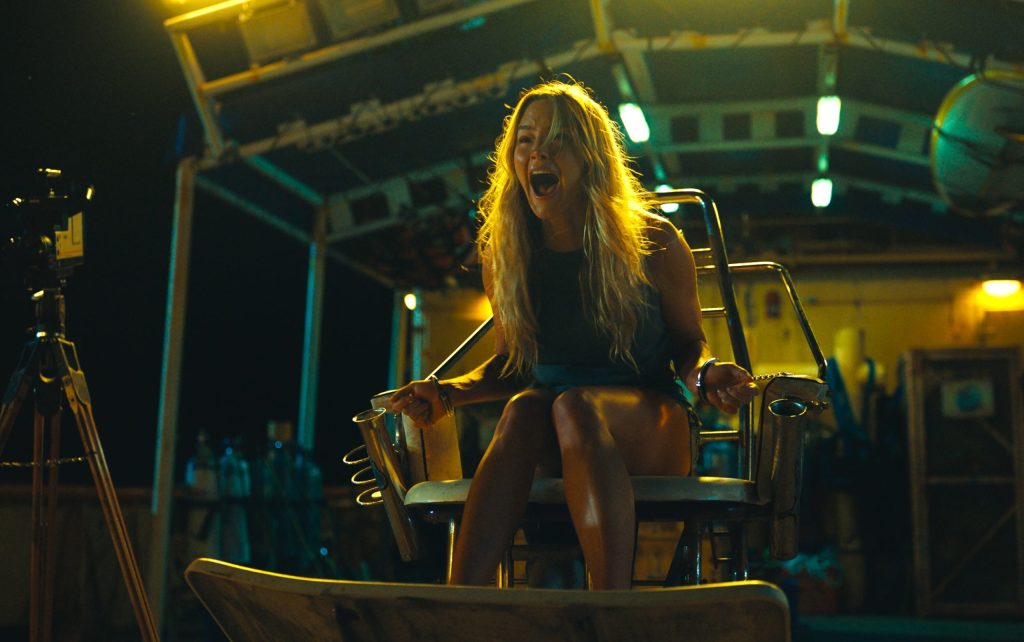 Zephyr (Hassie Harrison) cuffed to a fishing chair on the boat. She is screaming.