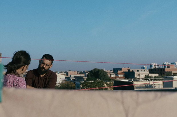 Raqi's disciple (Akram Dieghim) talking to Waffa (Hanaa Mansour) as she hangs up the laundra on the rooftop.