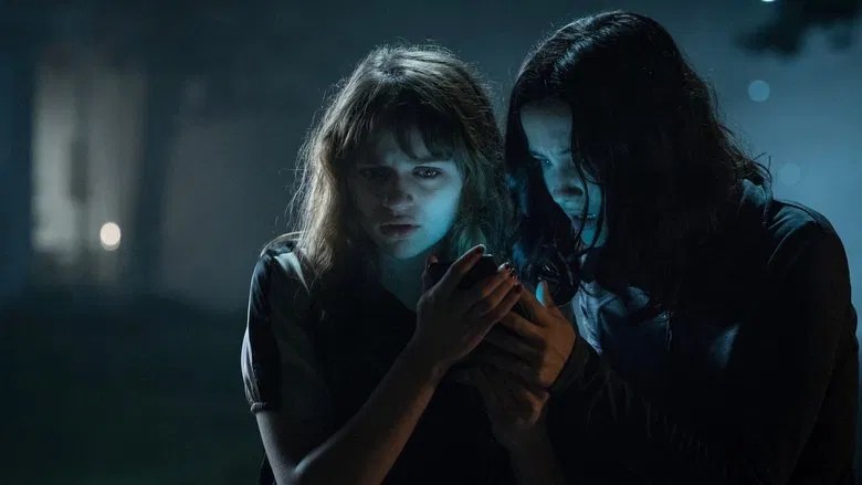 Hallie (Julia Goldanie Telles) and Wren (Joey King) huddled around a phone outside at night.