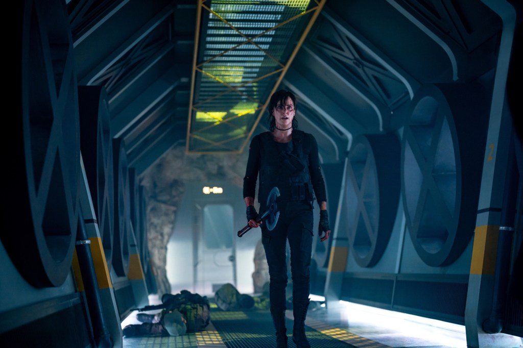 Andy (Charlize Theron) walking through a corridor that appears to be underground, holding an axe. There are bodies of soldiers behind her.