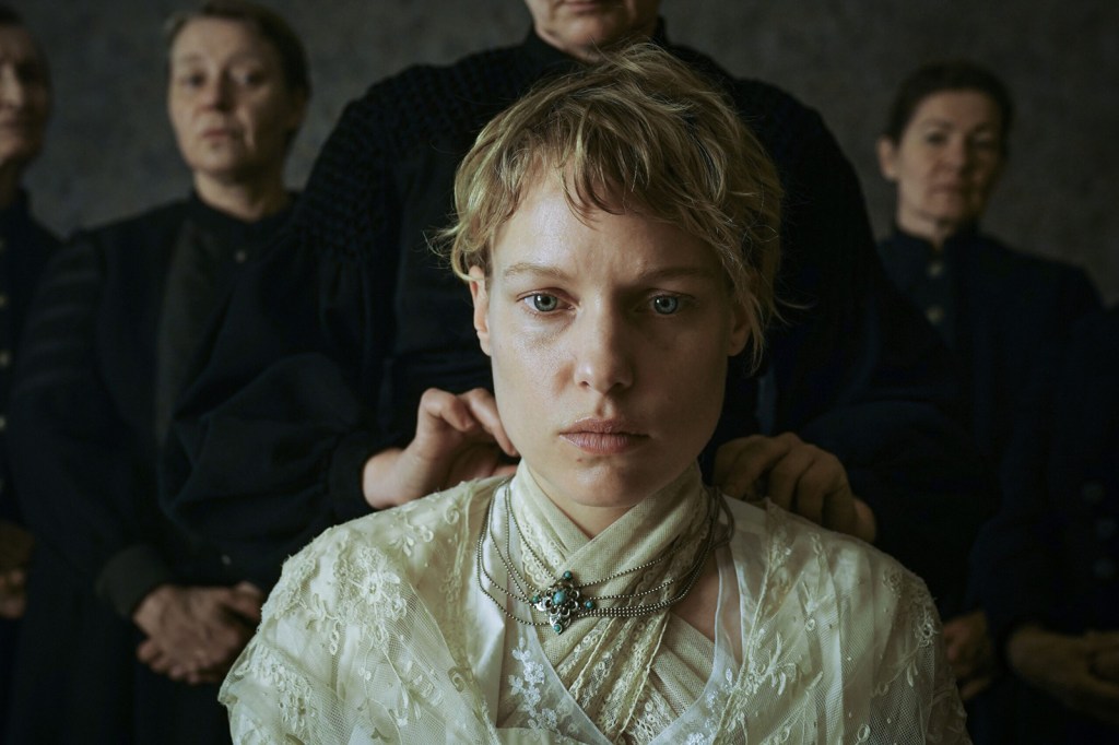 Judith (Julia Franz Richter) in an elaborate white dress. Somebody is putting a necklace on her. She looks frozen, shocked. 